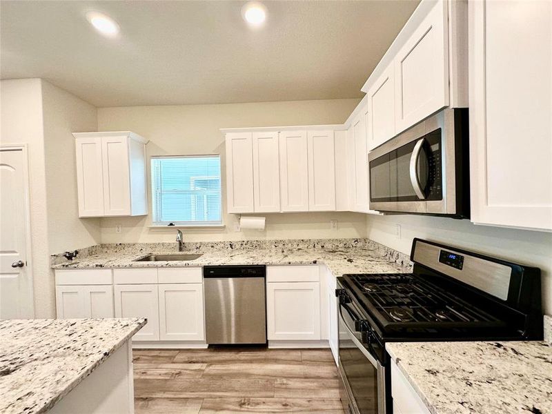Kitchen with white cabinetry, light hardwood / wood-style flooring, appliances with stainless steel finishes, light stone counters, and sink