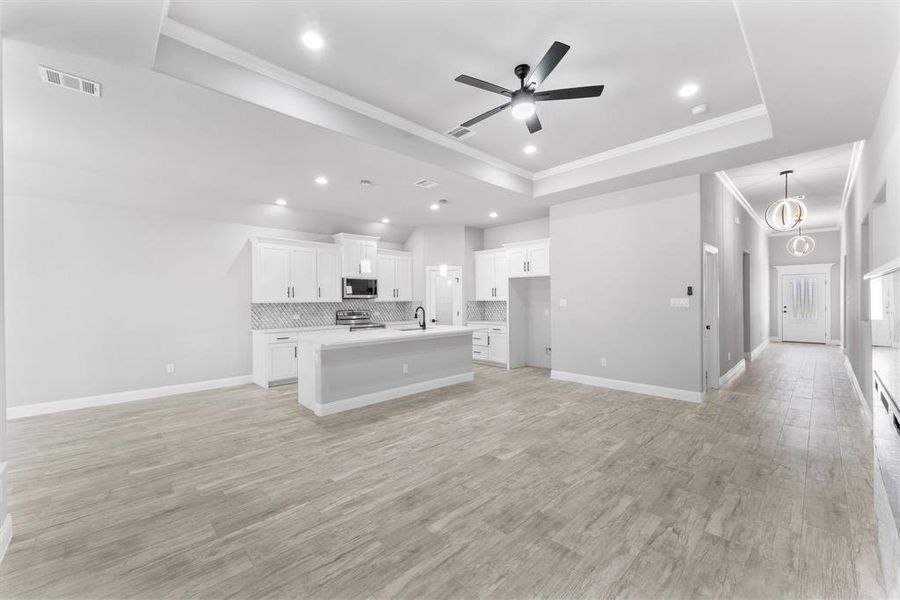 Kitchen with a kitchen island with sink, white cabinets, light hardwood / wood-style flooring, stainless steel appliances, and backsplash