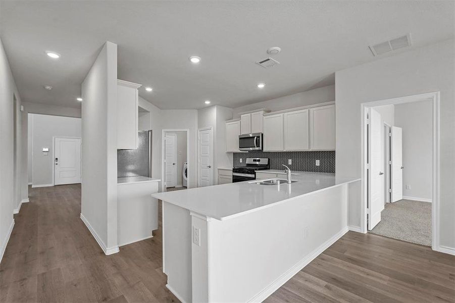 Kitchen with appliances with stainless steel finishes, kitchen peninsula, white cabinets, hardwood / wood-style flooring, and decorative backsplash