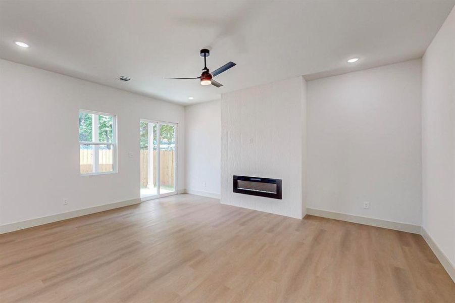 Unfurnished living room with ceiling fan, heating unit, light hardwood / wood-style floors, and a large fireplace