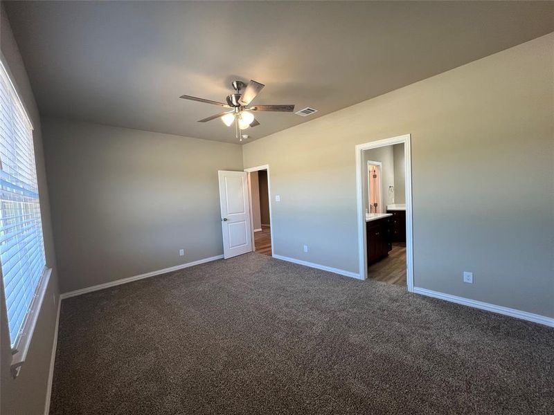 Unfurnished bedroom featuring ensuite bath, ceiling fan, and dark colored carpet