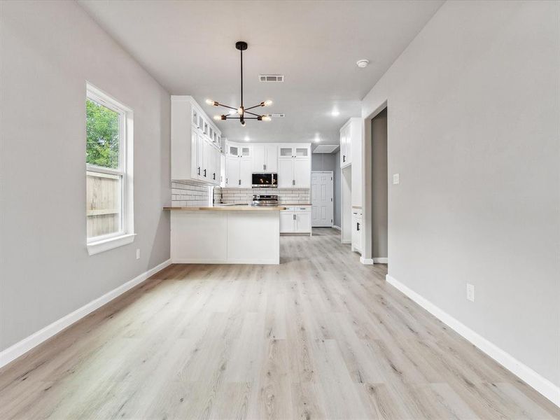 Kitchen featuring white cabinetry, light hardwood / wood-style flooring, a chandelier, kitchen peninsula, and decorative backsplash