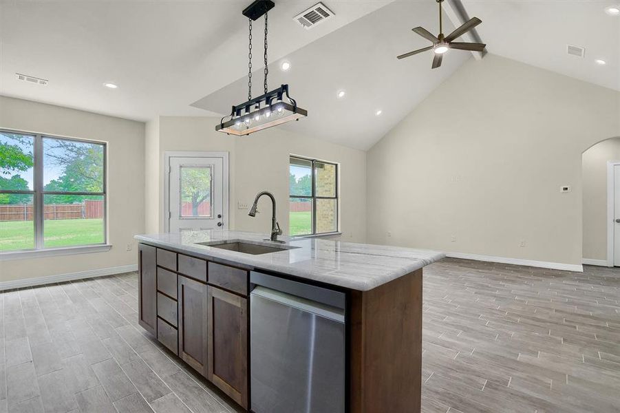 Kitchen with stainless steel dishwasher, decorative light fixtures, Tile Plank flooring, sink, and a kitchen island with sink