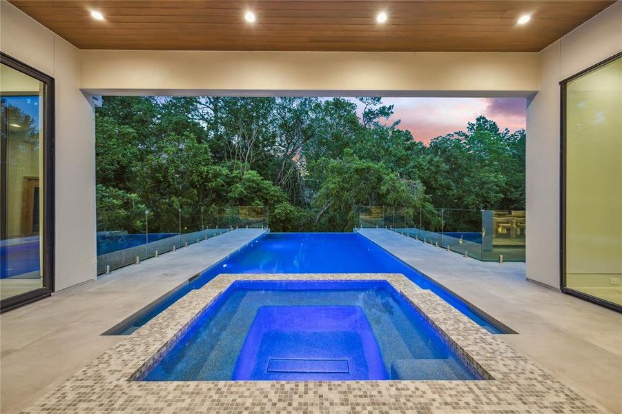 Take a dip in the sparkling heated pool with an infinity edge and spa, surrounded by lush landscaping, while blackened steel sconces illuminate the space and a massive covered porch, equipped with in-ceiling speakers, offers the ideal setting for enjoying the outdoors in style and comfort.