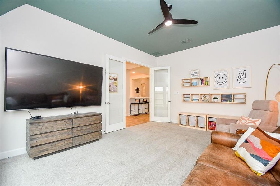 Spacious, well-lit game room featuring a vaulted ceiling with a contrasting paint accent, large windows providing ample natural light, double doors with glass accent. New carpet creates a clean, inviting space. a ceiling fan.