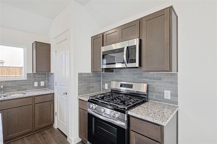 Kitchen with lofted ceiling, decorative backsplash, appliances with stainless steel finishes, and dark hardwood / wood-style flooring