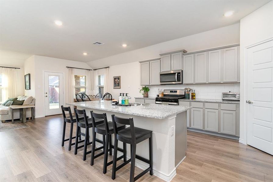 Kitchen featuring gray cabinetry, stainless steel appliances, a center island with sink, a breakfast bar, and light wood-type flooring