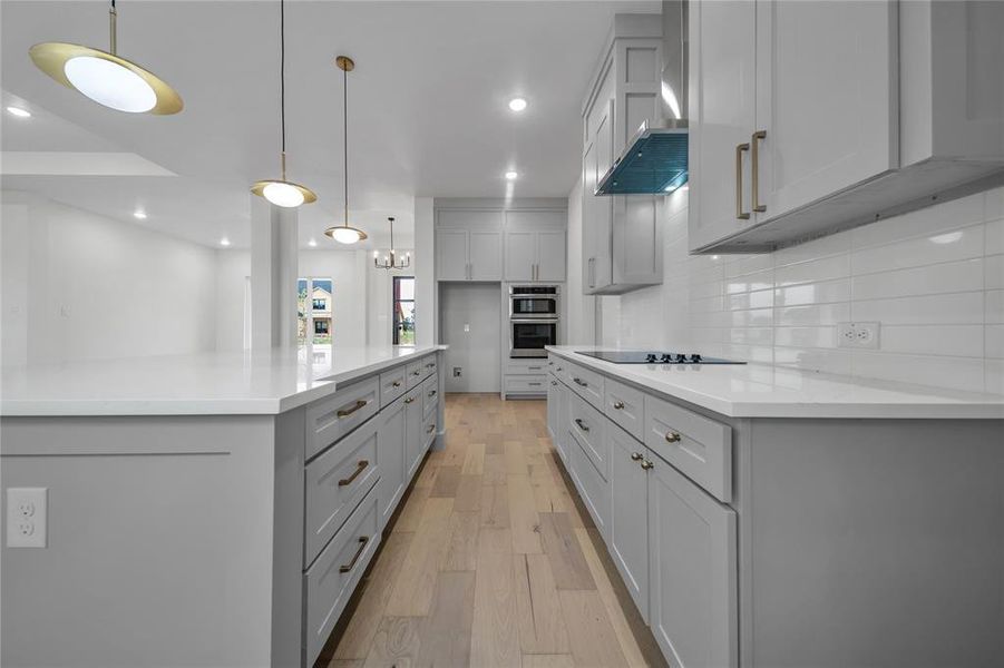 Kitchen with gray cabinets, decorative light fixtures, wall chimney exhaust hood, light hardwood / wood-style flooring, and backsplash