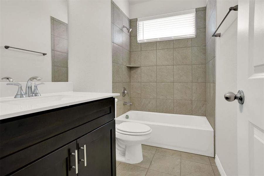 Full bathroom with tiled shower / bath combo, tile flooring, toilet, and vanity