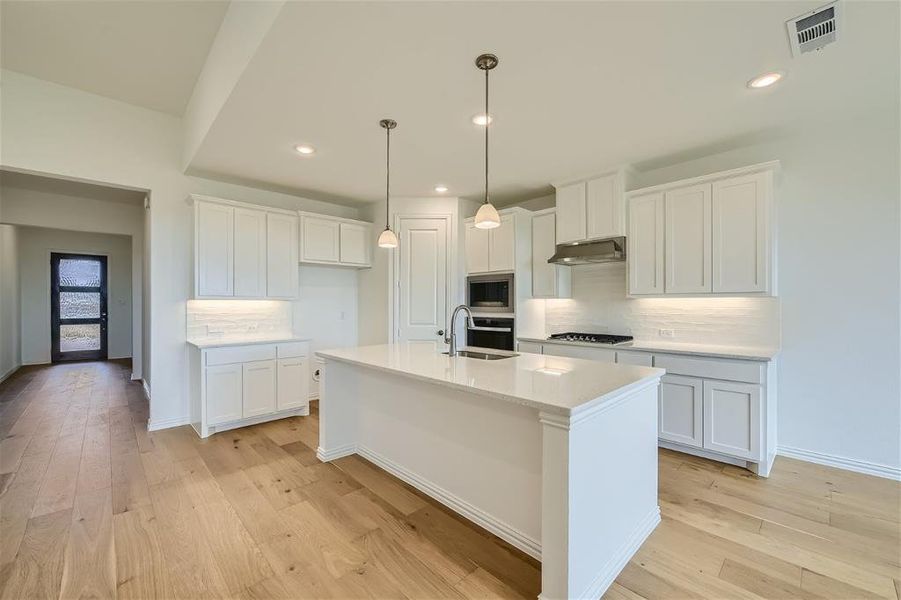 Kitchen with light wood-type flooring, a center island with sink, appliances with stainless steel finishes, backsplash, and extractor fan