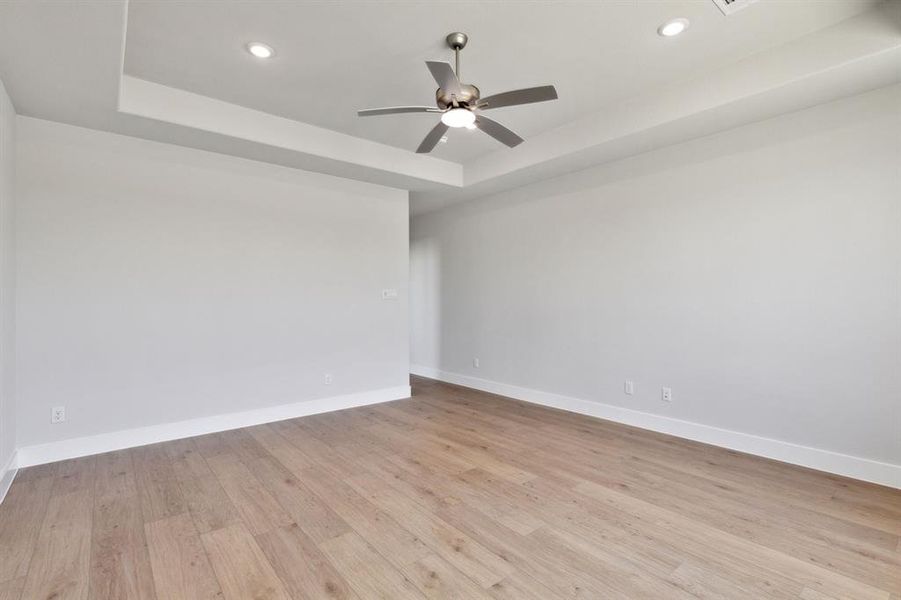Spare room with ceiling fan, light wood-type flooring, and a tray ceiling