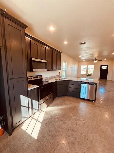 Kitchen with light stone countertops, stainless steel appliances, dark brown cabinets, ceiling fan, and sink