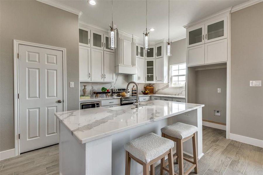 Kitchen with an island with sink, light stone counters, white cabinets, pendant lighting, and crown molding