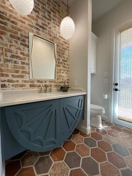 Bathroom with vanity, toilet, and brick wall