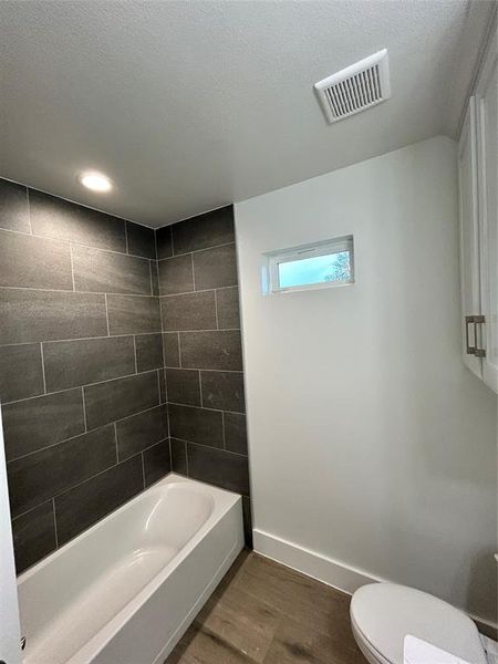 Bathroom with toilet, tiled shower / bath combo, hardwood / wood-style flooring, and a textured ceiling