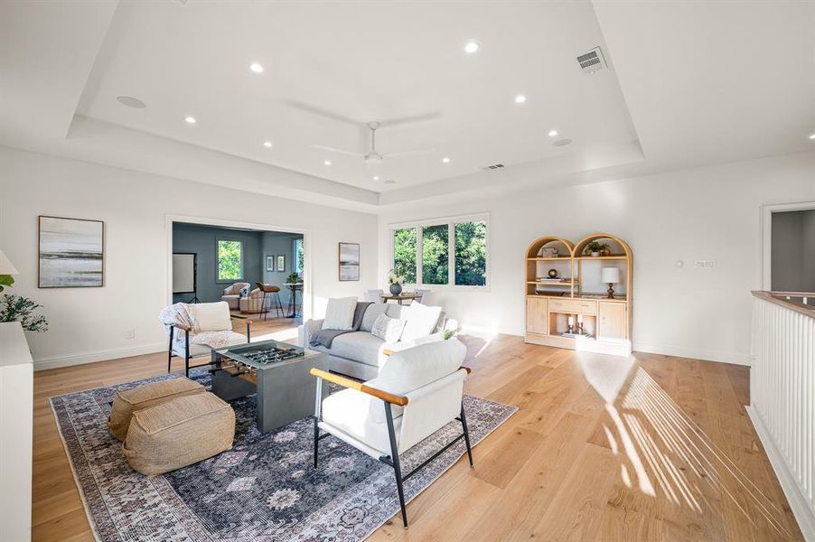 Living room with light hardwood / wood-style flooring, a raised ceiling, and plenty of natural light