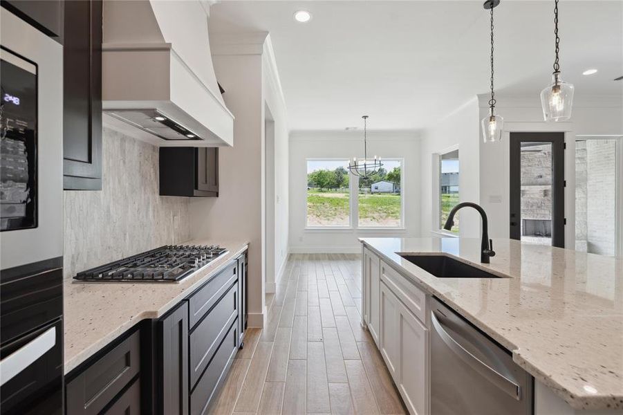 Kitchen featuring stainless steel appliances, sink, hanging light fixtures, custom range hood, and white cabinets