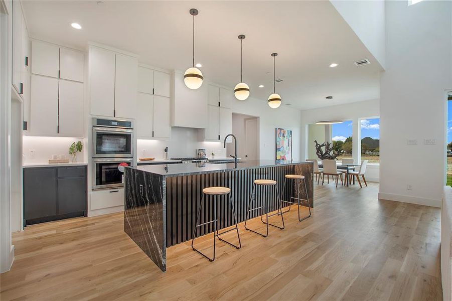 Kitchen featuring light wood-type flooring, a kitchen breakfast bar, white cabinetry, stainless steel double oven, and a kitchen island with sink