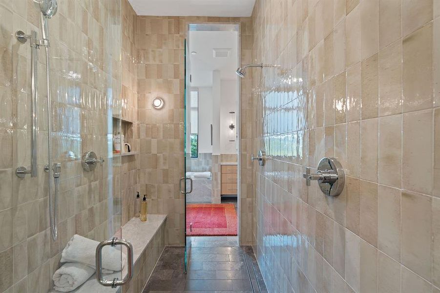 The walkthrough walk-in shower provides wall-length bench seating, full tile surround, and multiple shower heads.